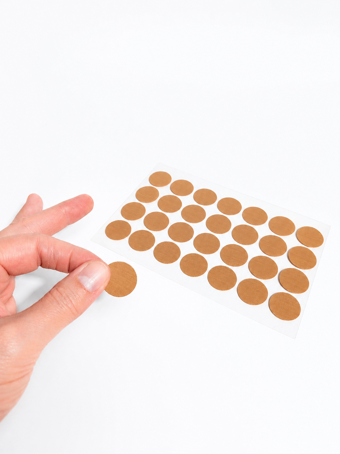 Hand interacting with adhesive duct tape disc patches on a white background